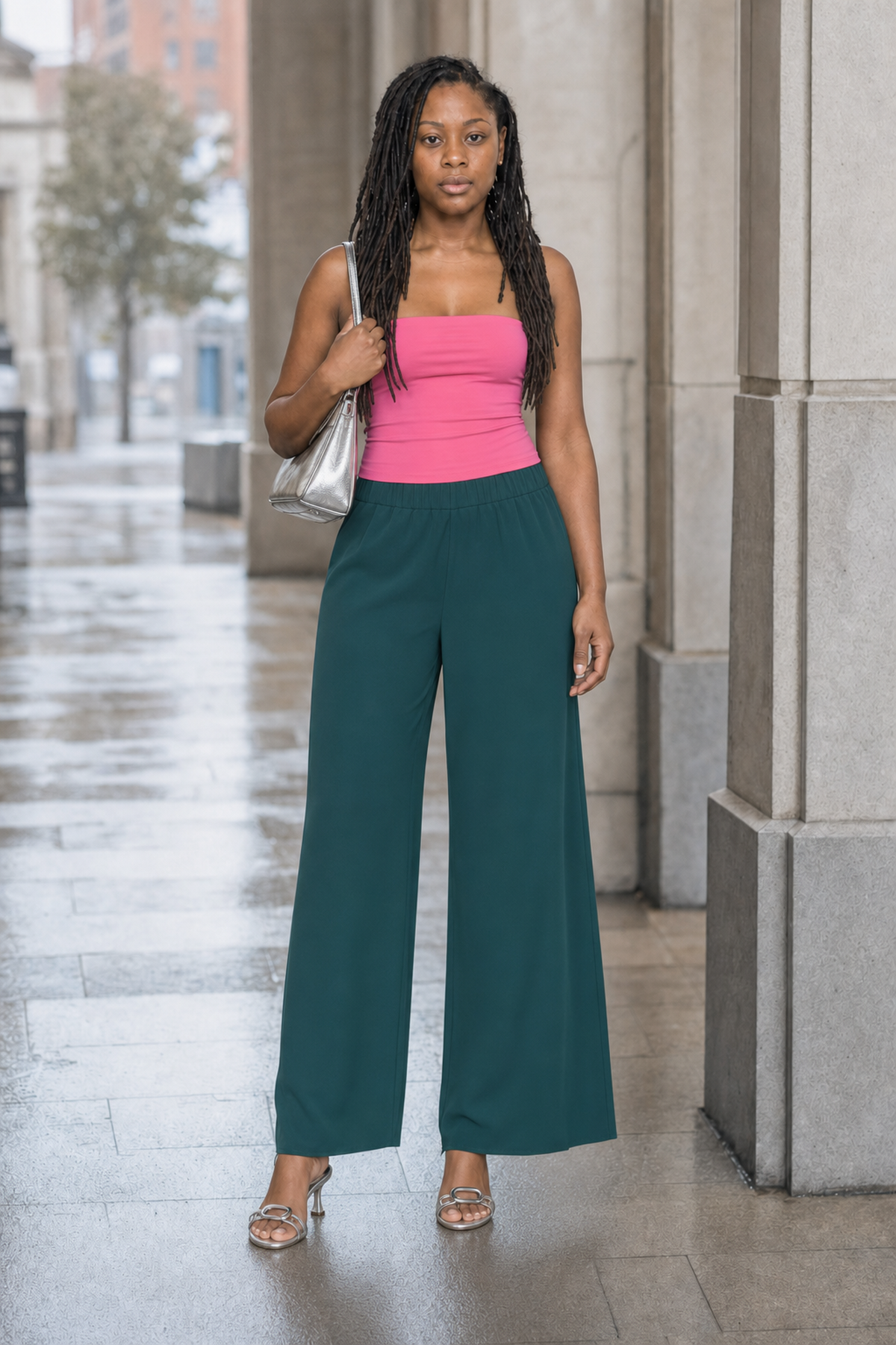 Full-body editorial photograph of Noelle in a Jellybean Pink Aritzia Contour tube top with Scarab green Babaton Strive trousers, a silver crescent shoulder bag and silver slingback sandals